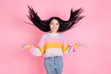 photo of young beautiful smiling charming asian girl with flying hair advertising shampoo isolated on pink color background