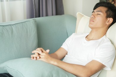 tired exhausted lazy asian young man teenager sleeping resting napping on sofa at home