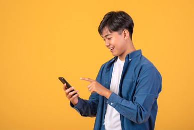 image asian man standing on orange background using a mobile phone.