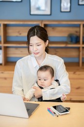 a woman holding a baby and operating a laptop