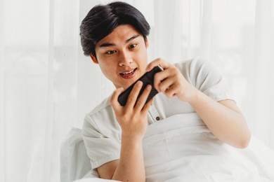 asian man is using his phone to play games in bed
