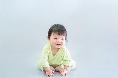 asian happy cute baby smiling, sitting on gray background. 6 months baby in green cloth on copy space as concept of bedroom, development, health, mood and motion of baby and kid department in hospital