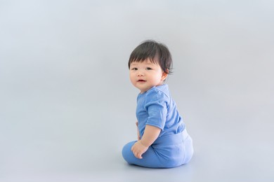 asian happy cute baby smiling, sitting on gray background. 6 months baby in blue cloth on copy space as concept of bedroom, development, health, mood and motion of baby and kid department in hospital