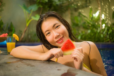 beautiful asian woman enjoying luxury holidays trip - young attractive and happy korean girl in bikini relaxed at tropical villa resort swimming pool eating fresh watermelon