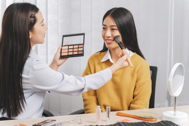 asian professional make-up artist working at beauty salon blending eyeshadow on face of a female client.