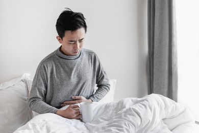 young man sitting on the bed with hands covering his stomach
