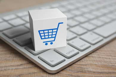 shopping cart flat icon on white block cube with modern computer keyboard on wooden table, business shop online concept