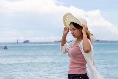 portrait of asian women with white hat walking on the beach  with  sea background. asian girl travel in the summer.