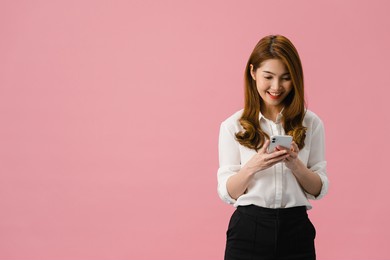 young asia lady using phone with positive expression, smiles broadly, dressed in casual clothing feeling happiness and standing isolated on pink background. happy adorable glad woman rejoices success.