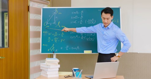 asian senior high school male teacher teach math online through laptop in classroom