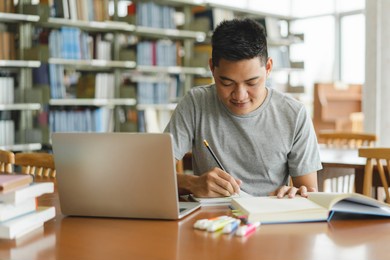male asian student studying and reading book in library