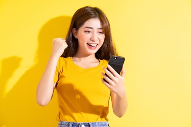 young asian girl uisng smartphone on yellow background