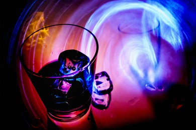 a glass of green drink with ice on a glass table on the vibrant neon colors background.