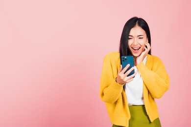 happy asian portrait beautiful cute young woman teen smiling excited using smart mobile phone studio shot isolated on pink background, thai female surprised making winner gesture on smartphone