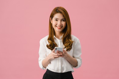 surprised young asia lady using mobile phone with positive expression, smiles broadly, dressed in casual clothing and looking at camera on pink background. happy adorable glad woman rejoices success.