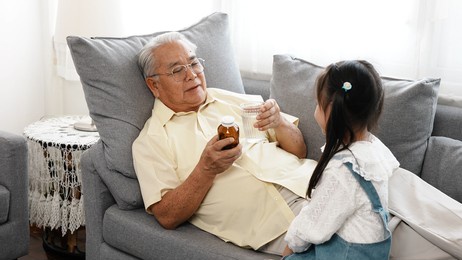 happy family little asian daughter carried a drug and glass of water to the sick grandfather on the sofa in the house take care, elderly old man patient retired enjoy life concept.