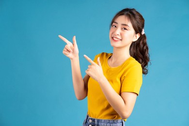young asian woman using finger to pointing on blue baclground
