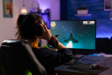 focused gamer puts professional headphones and playing space shooter videogames use modern equipment for digital tournament. pro player sitting on gaming chair streaming video games using rgb keyword