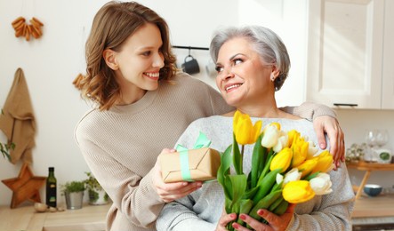 positive elegant elderly woman with bunch of fresh tulips smiling and accepts a gift from a young daughter during a mother's day celebration