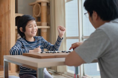 asian child and his father playing chinese go game board in living room
