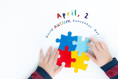 "world autism awareness day - april 2" top view - hands of a young autistic boy playing with colorful puzzles pieces on white table. kids mental health concept. autism spectrum disorder, supportive.