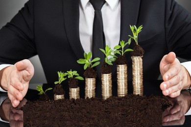 midsection of businessman's hands protecting coins in saplings representing responsible business