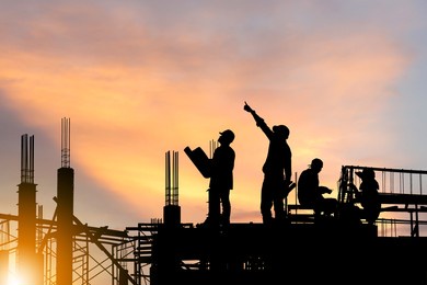 silhouette of engineer and worker on building site, construction site at sunset in evening time.