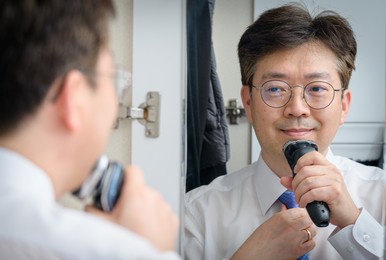 middle-aged asian businessman shaving in the morning looking in the mirror.
