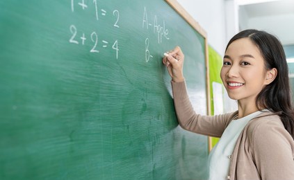 closeup portrait of young happy asian teacher write on chalk board. woman writing on blackboard wall. idea creative education teaching math and spelling letter, knowledge, back to school concept