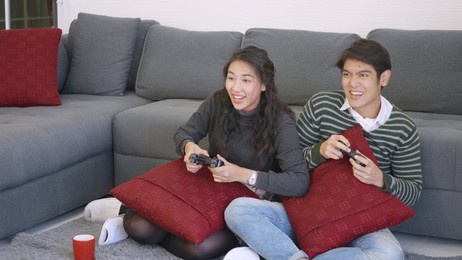 happy asian beautiful young family couple husband and wife smile and laugh enjoying funny with each other playing video game, holding joysticks console. happiness and gaming concept.