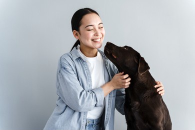 nice affectionate woman petting a dog and laughing on a gray background. cheerful girl playing with her pet.
