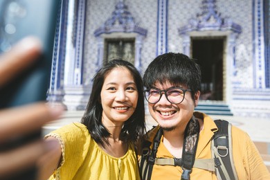 happy smile asian married adult traveller love couple. summer vacation outdoor travel in asia temple background on day. man and woman has selfie by smartphone with yellow shirt, dress. thailand