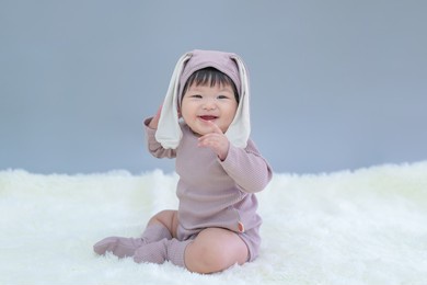 easter bunny, baby in rabbit cloth. asian happy baby smiling, sitting on gray background. cute 6 months baby start sitting with copy space as easter concept, baby or kid department in hospital