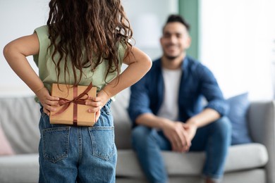 little girl greeting her dad with fathers day, holding gift behing back