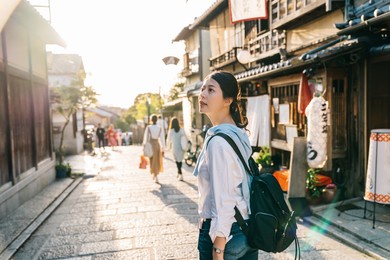 traveler stopped on the street and looking at the japanese traditional building. japan travel tourist woman on vacation in kyoto shopping in alley. cheerfully visit kyoto.