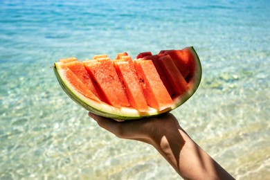 hand holding slice of watermelon on the beach. sea and blue sky background. summer mood. 2021
