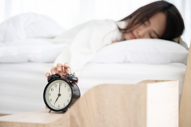 young asian woman wake up early in morning. she lying on bed and trying turn off alarm clock