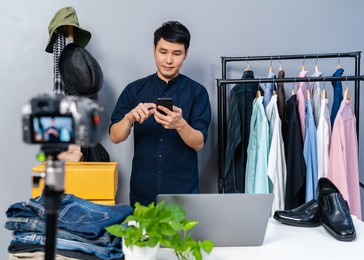 young man selling clothes and accessories online by using smartphone and camera live streaming, business online e-commerce at home