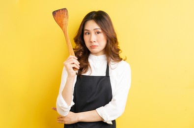 beautiful housewife holding spoon of rice isolated on yellow background