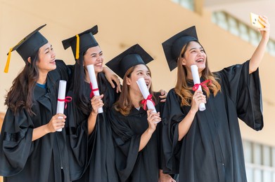 happy group of graduates asian student in academic gown and graduation cap holding diploma and take a selfie