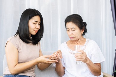 asian daughter giving pills to old mother helping her mom taking medicine with glass of water 