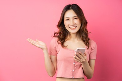 young asian girl using the phone on pink background