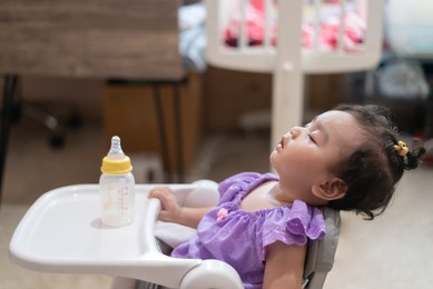side view of cute little asian baby girl sitting asleep on the dining table after eating full in the house