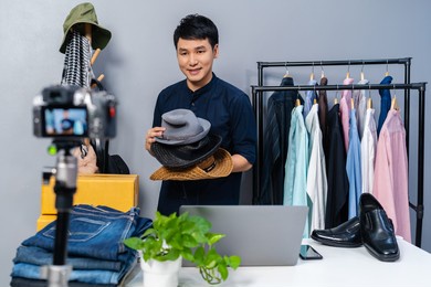 young man selling hat and clothes online by camera live streaming, business online e-commerce at home
