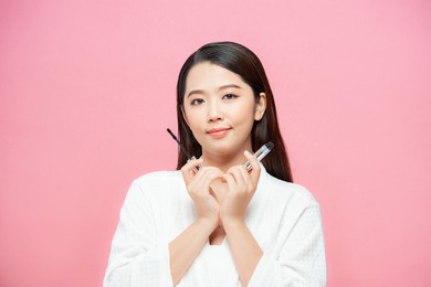 woman applying black mascara on eyelashes with brush over pink background with copy space