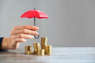 young woman hand holding small red umbrella over pile of coins on table. close up of stack of coins with female hands holding umbrella for protection. financial safety and investment concept.  