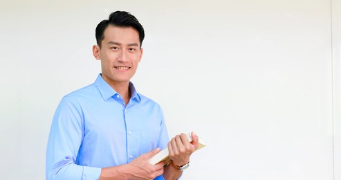 asian young male teacher holds a book and smiles at you in classroom