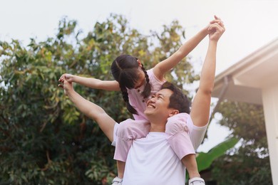 family asian happy little girl sit on dad's shoulder playing on the yard at home, portrait young father and dougther enjoy love hug.