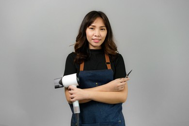 portrait of asian gorgeous cheerful young female professional hairdresser holding blowdryer smiling to the camera posing at her beauty studio. 