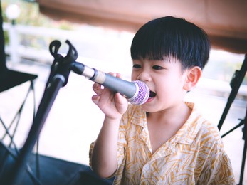 cute young asian boy singing into a microphone. happy kids singing into microphone